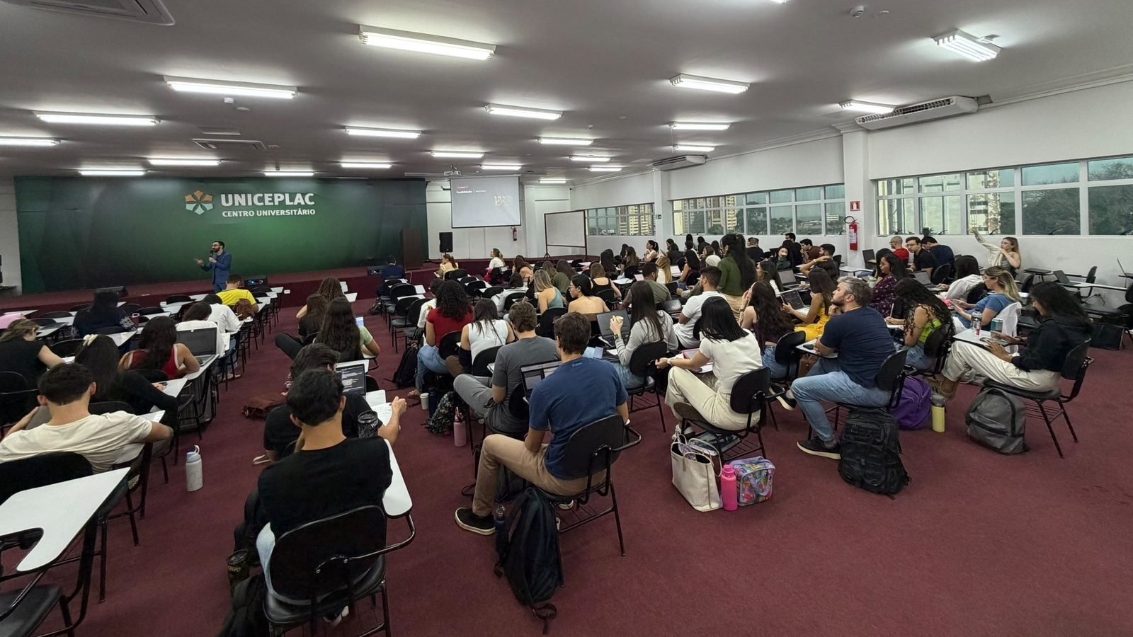 Mateus Cavarzan no palco da UNICEPLAC, falando para uma sala cheia de alunos
