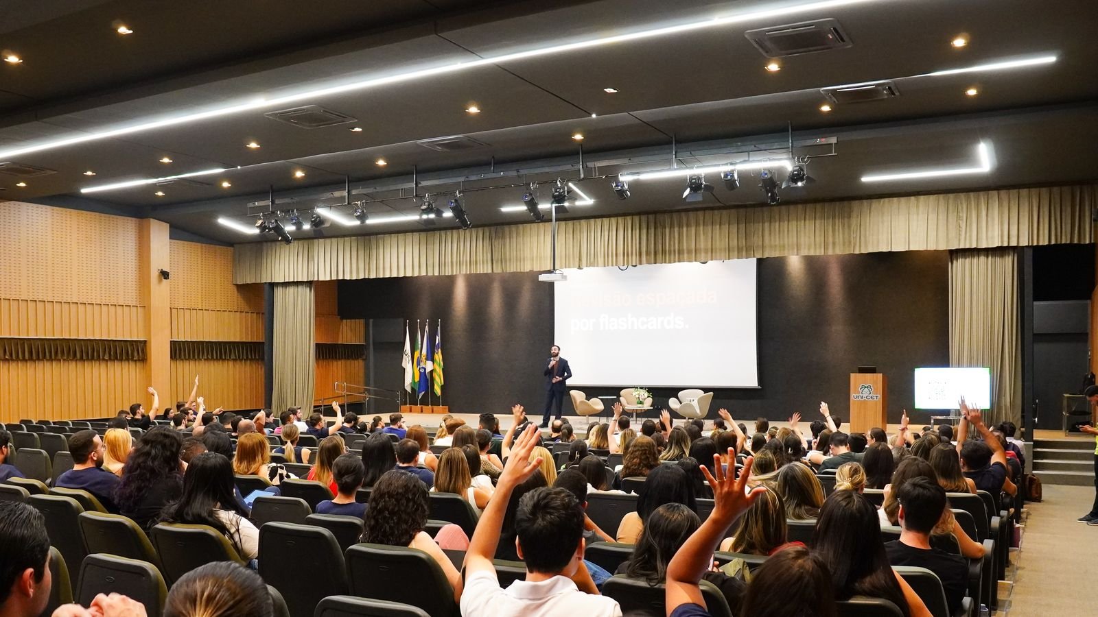 Auditório da UNICET lotado, com alunos de mãos levantadas, e Mateus Cavarzan no palco