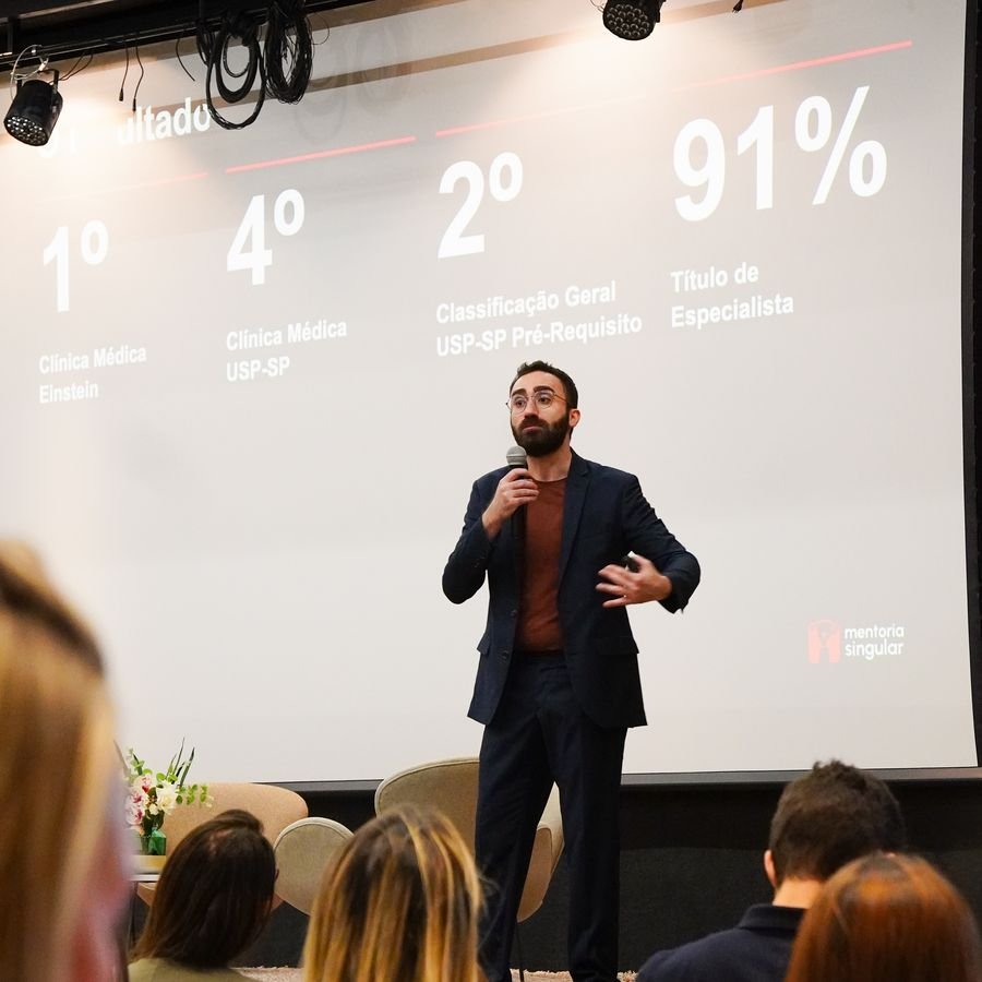 Mateus Cavarzan no palco, diante de um slide com resultados de aprovação