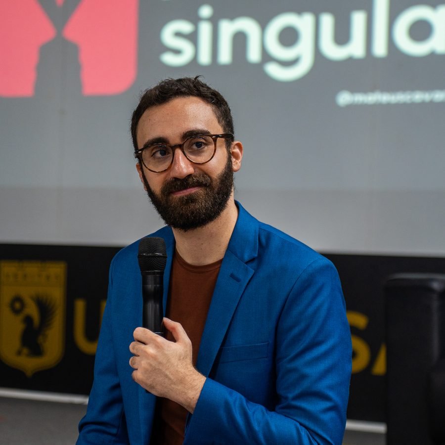 Mateus Cavarzan com o microfone, diante do telão da Mentoria Singular