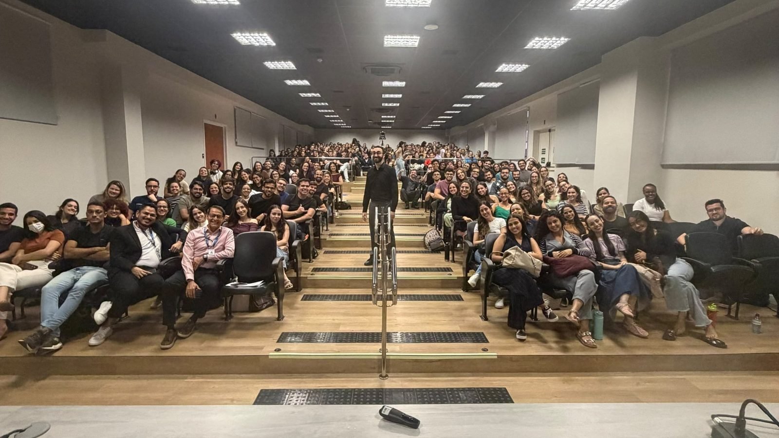 Mateus Cavarzan de pé no corredor do auditório da UNIT, com a plateia sorrindo ao redor