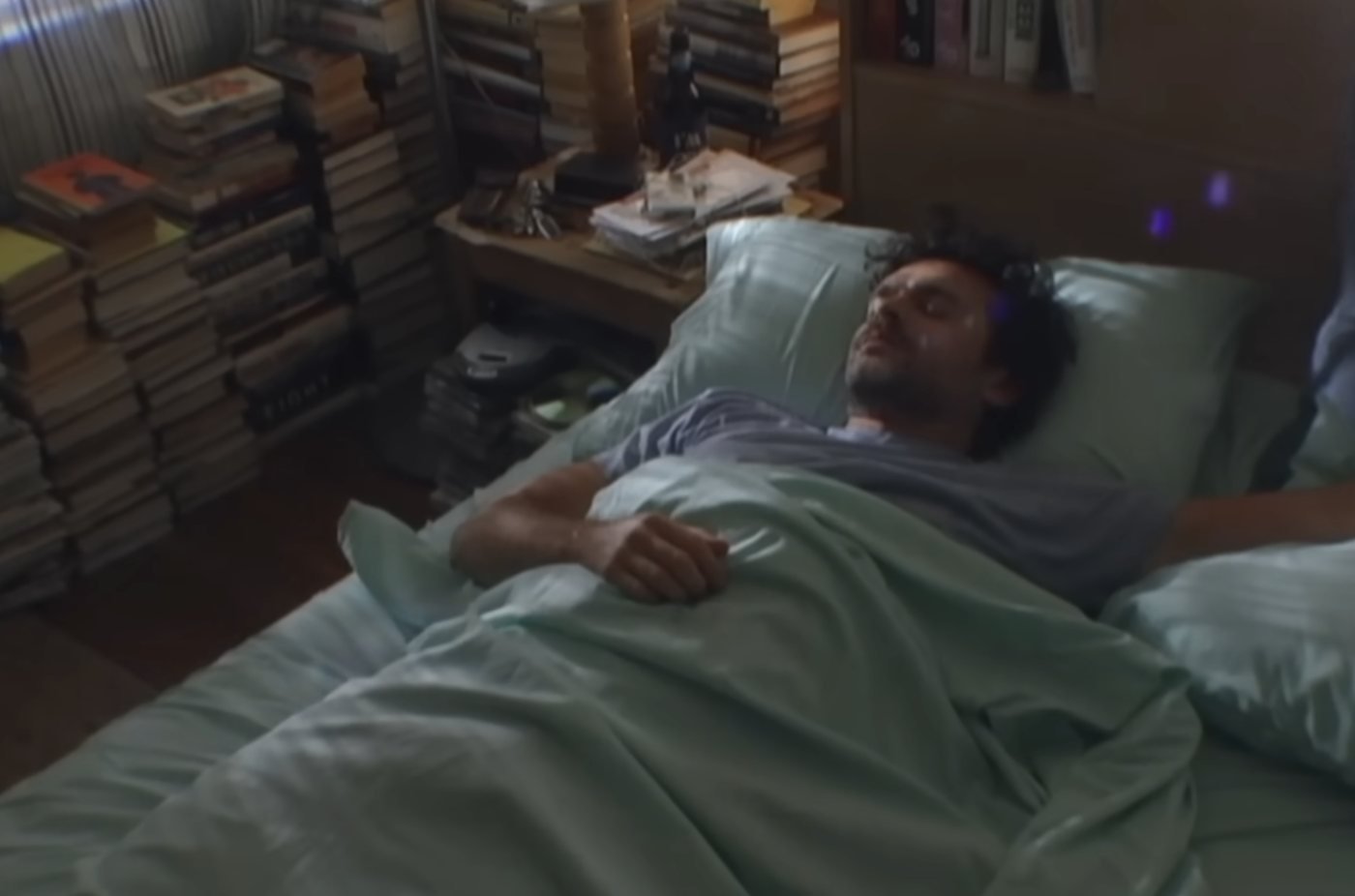 Cena do clipe: o homem deitado na cama, cercado de livros